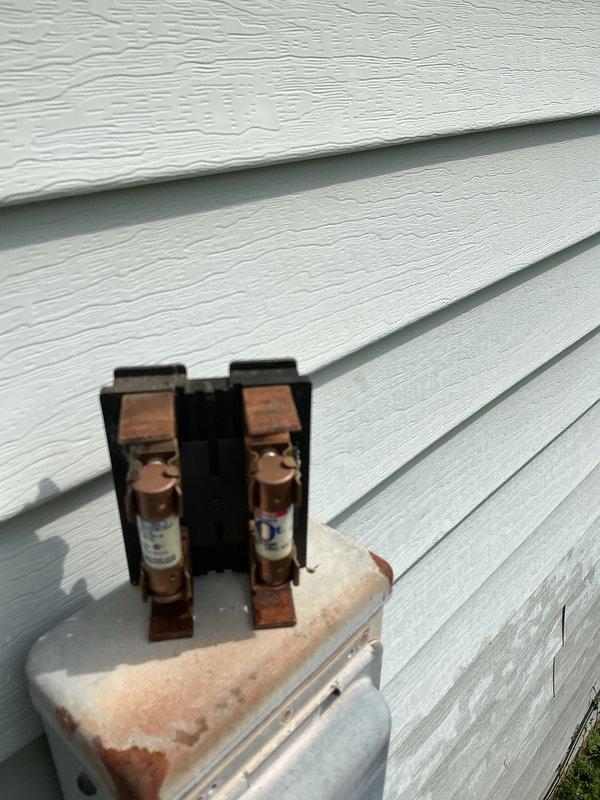 Completed standard AC tune-up service on residential cooling system. Inspected exterior disconnect box, noting significant rust and corrosion on housing and mounting components; fuses operational but enclosure shows weathering from moisture exposure. Evaluated outdoor condensing unit and associated refrigerant lines, electrical connections, and conduit routing along exterior wall.