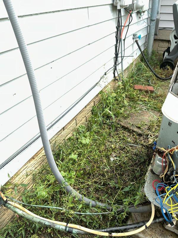 Completed standard AC tune-up service on residential cooling system. Inspected exterior disconnect box, noting significant rust and corrosion on housing and mounting components; fuses operational but enclosure shows weathering from moisture exposure. Evaluated outdoor condensing unit and associated refrigerant lines, electrical connections, and conduit routing along exterior wall.