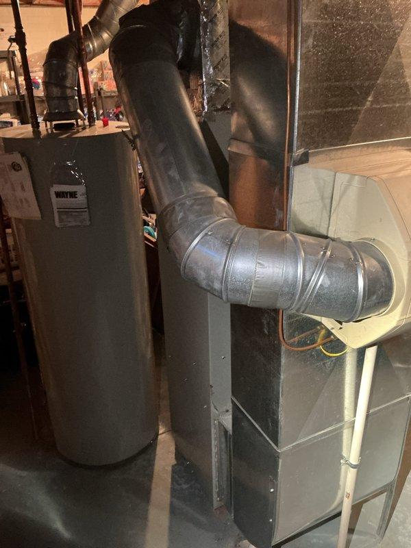 # HVAC Service Call - Air Conditioning System Not Cooling

Responded to service call for 26-year-old residential air conditioning system reported as not blowing cold air. Upon arrival, performed comprehensive diagnostic evaluation of both indoor and outdoor HVAC components.

Inspected basement-mounted air handler unit and associated ductwork for proper airflow and mechanical operation. Verified furnace/air handler cabinet integrity and examined flexible duct connections for air leakage or restrictions. Checked indoor coil accessibility and blower motor function.

Proceeded to outdoor condenser unit located on exterior gravel pad adjacent to building. Examined white condenser cabinet and protective top grille for damage or debris obstruction. Inspected electrical disconnect box and associated conduit connections for proper power supply. Evaluated refrigerant line connections, compressor operation, and condenser fan motor performance.

Conducted system performance testing including tempe