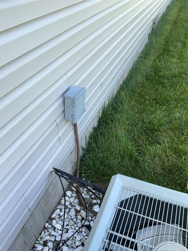 # HVAC Service Call - Air Conditioning System Not Cooling

Responded to service call for 26-year-old residential air conditioning system reported as not blowing cold air. Upon arrival, performed comprehensive diagnostic evaluation of both indoor and outdoor HVAC components.

Inspected basement-mounted air handler unit and associated ductwork for proper airflow and mechanical operation. Verified furnace/air handler cabinet integrity and examined flexible duct connections for air leakage or restrictions. Checked indoor coil accessibility and blower motor function.

Proceeded to outdoor condenser unit located on exterior gravel pad adjacent to building. Examined white condenser cabinet and protective top grille for damage or debris obstruction. Inspected electrical disconnect box and associated conduit connections for proper power supply. Evaluated refrigerant line connections, compressor operation, and condenser fan motor performance.

Conducted system performance testing including tempe