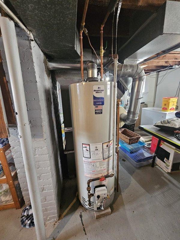 Installed a 40-gallon Bradford White standard tanked water heater in basement mechanical area, positioning unit on brick platform per customer request for elevated placement. Connected copper supply lines, gas valve assembly, and integrated all plumbing connections to existing overhead infrastructure, ensuring proper venting and code-compliant installation on concrete floor.
