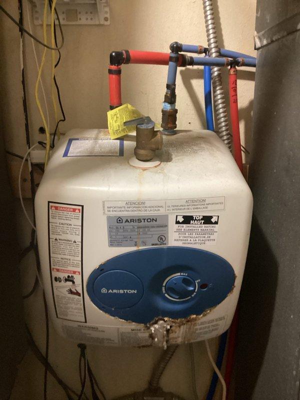 Conducted comprehensive site assessment for complete HVAC system and water heater replacement at commercial property with ground-level equipment installation. Evaluated existing Ariston brand water heater with blue control panel and standard plumbing connections including hot and cold water lines with brass valves and fittings. Assessed current furnace unit with metal paneling, flexible metal conduit connections, and associated ductwork. Documented all equipment specifications, manufacturer labels, and existing utility configurations including electrical wiring, PVC drainage lines, and mechanical room layout to provide accurate replacement estimate for full system upgrade.
