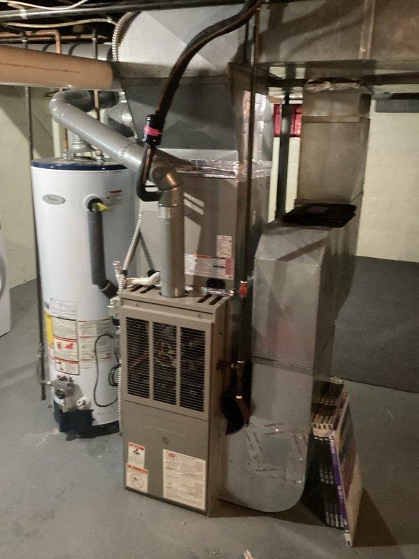 Conducted comprehensive assessment of existing residential HVAC system located in basement utility area for furnace replacement estimate. Evaluated current beige/tan furnace unit with front ventilation grille, documented equipment specifications, and photographed existing installation including adjacent water heater, ductwork configuration, refrigerant lines, and electrical connections. Assessed spatial constraints, existing duct system compatibility, and utility connections to provide accurate replacement recommendations for new furnace installation.