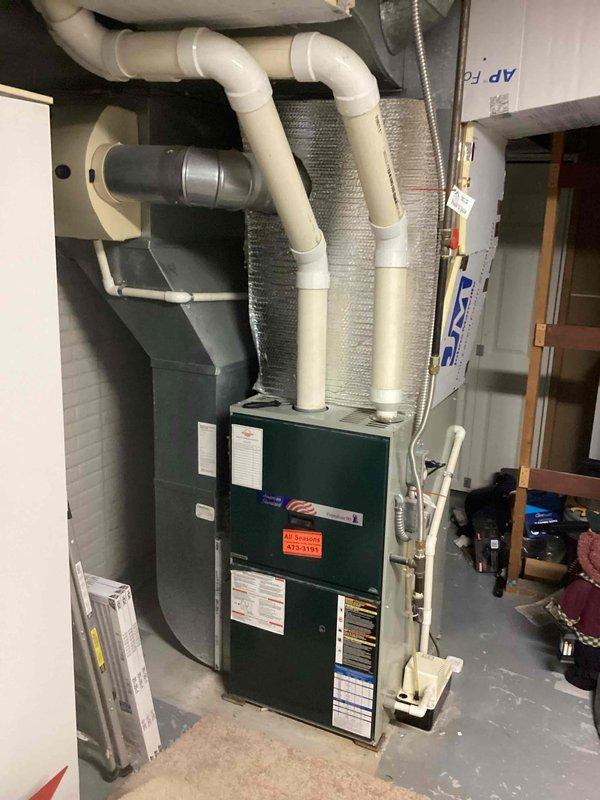 Completed comprehensive estimate for full HVAC system replacement including outdoor condenser unit and indoor furnace assembly. The existing equipment showed significant age and weathering, with the outdoor condenser unit displaying surface discoloration and dirt accumulation on its cabinet and louvers. Assessed current system configuration including electrical disconnect box, service panel connections, and metal conduit routing on exterior brick wall installation. Evaluated indoor green furnace unit with associated white PVC intake and exhaust venting system, insulated flexible ductwork, copper refrigerant line sets, and mounting hardware in basement mechanical room. Documented equipment specifications, venting configurations, and electrical service requirements. Photographed both indoor and outdoor components to provide detailed assessment for complete system replacement proposal.