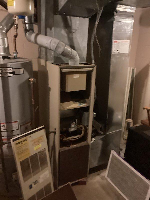 Conducted comprehensive assessment of existing HVAC system for complete furnace and air conditioning replacement. Evaluated outdoor condensing unit showing signs of weathering and age, with displaced top panel and visible deterioration on exterior surfaces. Unit currently positioned on ground level against building exterior with electrical conduit connection to wall-mounted junction box. Assessed indoor equipment configuration including furnace with accessible internal components, air handler, and associated ductwork and PVC venting systems. Documented current system layout, electrical connections, refrigerant line routing, and condensate drainage infrastructure. Provided detailed replacement estimate covering removal of existing equipment and installation of new high-efficiency furnace and air conditioning system sized appropriately for the residence.
