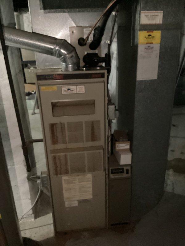 Conducted comprehensive assessment of existing HVAC system in residential basement for furnace replacement estimate. Evaluated current beige/tan cabinet-style furnace unit with front-access filter panels and associated ductwork connections. Inspected flexible metallic ductwork, rigid piping connections, and adjacent dark cabinet air handler unit. Documented equipment configuration, spatial constraints, and installation conditions through detailed photography. Assessed concrete floor surface, wall clearances, and existing duct routing to determine optimal replacement specifications and installation requirements.