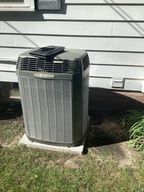 Completed full HVAC system replacement including outdoor Trane condenser unit and indoor furnace with air handler. The new condenser was installed on existing concrete pad against exterior wall with proper clearances maintained, refrigerant lines were run and insulated, and all electrical connections completed. Indoor installation included new furnace with viewing window, wall-mounted air handler, PVC condensate drain lines, humidifier unit, and metallic supply ductwork with all components properly integrated and tested for operation.