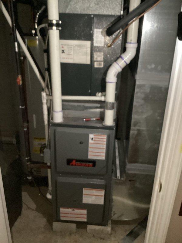 Completed comprehensive estimate for full HVAC system replacement at residential property. Evaluated existing Amana furnace installation located in basement utility area with interconnected air handler and evaporator coil assembly. Assessed current system configuration including white PVC condensate drainage piping, ductwork connections, and ventilation components within confined mechanical space. Inspected outdoor condensing unit positioned on concrete pad against home exterior with proper clearances from structure. Unit currently installed in mulched area adjacent to white vinyl siding with electrical service panel and meter mounted above on exterior wall. Documented complete system layout including refrigerant line set routing, electrical connections, and overall equipment condition. Photographed indoor furnace assembly showing vertical installation with top-mounted coil configuration and multiple PVC pipe connections for combustion air and condensate removal. Captured outdoor unit 
