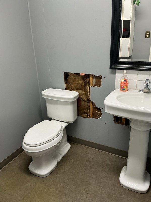 Accessed plumbing system through wall cavity between toilet and pedestal sink to address water damage and deterioration. Removed section of drywall to expose wooden framing studs and assess extent of damage to interior wall materials. Located and inspected black vertical drain pipe and metal ductwork within wall cavity. Removed and reinstalled affected plumbing components to resolve issue. Documented existing water staining and structural deterioration for repair assessment.