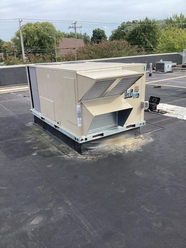 Successfully completed installation of a commercial packaged rooftop HVAC unit on a flat membrane roof. The new beige/tan RTU was properly mounted on a curb adapter platform with the condenser coil positioned for optimal airflow and service access. Unit installation included proper placement and securing to existing rooftop infrastructure in accordance with manufacturer specifications and commercial building codes.