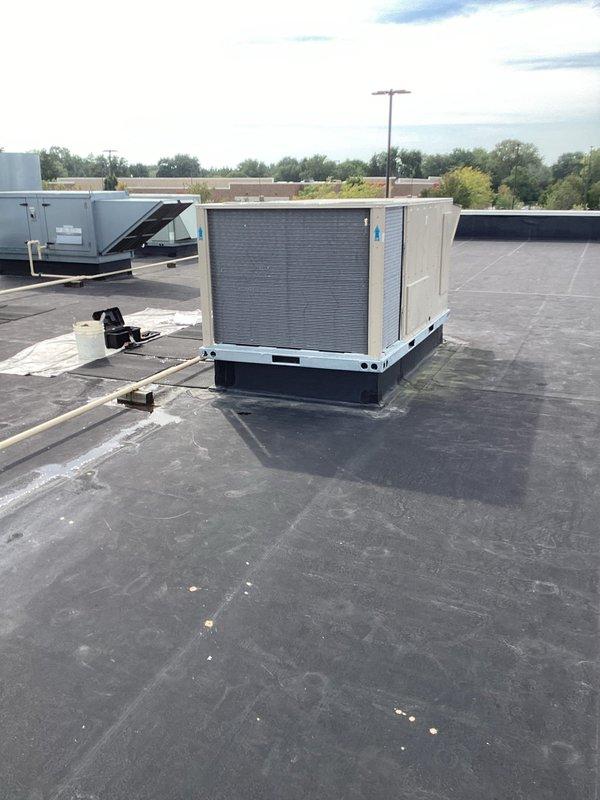 Successfully completed installation of a commercial packaged rooftop HVAC unit on a flat membrane roof. The new beige/tan RTU was properly mounted on a curb adapter platform with the condenser coil positioned for optimal airflow and service access. Unit installation included proper placement and securing to existing rooftop infrastructure in accordance with manufacturer specifications and commercial building codes.