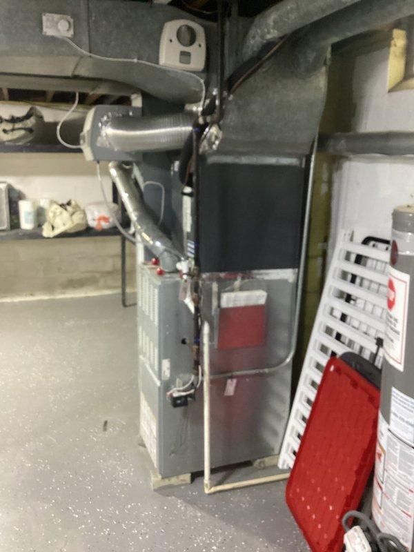Completed comprehensive HVAC system evaluation in residential basement mechanical room for equipment replacement estimate. Assessed existing gray furnace unit with metal ductwork, water heater, and associated mechanical systems including piping, electrical connections, and ventilation components. Documented current equipment configuration, spatial layout, and infrastructure conditions including exposed ceiling joists with fiberglass insulation, utility routing through ceiling space, and concrete block wall construction to provide accurate replacement recommendations.