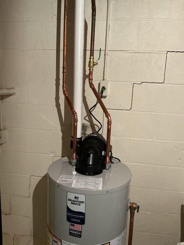 Responded to service call for leaking water heater. Upon arrival, performed visual inspection of tanked water heater unit and surrounding plumbing connections. Verified water heater installation alignment using level to check for proper positioning, as improper leveling can contribute to tank stress and potential leak points. Inspected copper supply lines, brass fittings, valves, and PVC drain connections for signs of moisture or active leaking. Documented existing conditions including water heater placement, piping configuration, and circulator pump mounted on top of unit. Photographed installation for service records showing vertical pipe runs along wall and connection points to tank.