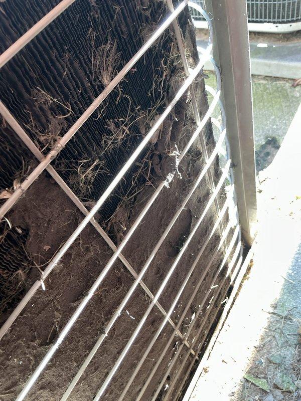 Responded to no cooling complaint on residential air conditioning system. Upon arrival, found outdoor condenser unit with heavily restricted airflow due to significant accumulation of organic debris (grass clippings, leaves, twigs, and branches) lodged in condenser coils. Removed protective grille and thoroughly cleaned condenser coil fins, removing all debris buildup to restore proper airflow. System tested and confirmed cooling operation restored to normal parameters.