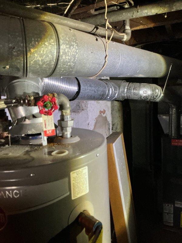 # Water Heater Replacement Estimate

Conducted on-site assessment of existing water heater installation located in basement utility area. Inspected current unit, a cylindrical tank-style water heater with visible manufacturer labeling and standard plumbing connections including shutoff valve and supply lines. Evaluated existing copper piping infrastructure, noting patina consistent with age and normal oxidation. Examined installation environment including overhead ductwork, structural joists, and concrete foundation to determine accessibility and any potential complications for replacement work.

Documented water heater configuration with red-wheeled gas shutoff valve, top-mounted connections, and proximity to HVAC ductwork system. Assessed clearance requirements and existing venting arrangements. Photographed current installation showing PVC and metal pipe connections, concrete floor mounting surface, and spatial constraints within mechanical room. Noted crawl space conditions includi