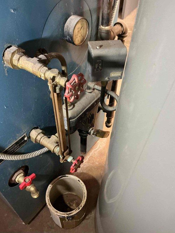 Responded to service call for leaking sight glass on 32-year-old hydronic heating system. Upon inspection, identified leaking glass tube assembly on boiler requiring immediate attention to prevent water damage. Discussed system age and replacement options with homeowner given the advanced age of the equipment and potential for additional component failures. Placed collection bucket beneath leak as temporary measure and documented existing conditions including aged copper piping, circulation pump, and pressure gauge assembly showing signs of corrosion and wear consistent with three decades of operation.