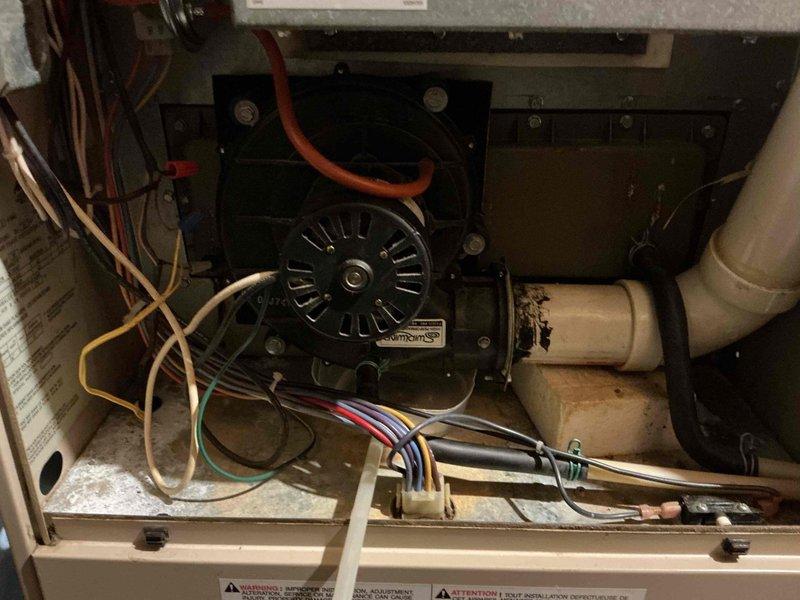 Responded to reported water leak originating from furnace condensation system. Upon inspection, identified active leaking from condensate collection box located behind the inducer blower assembly. Visual examination revealed significant rust and corrosion on metal mounting brackets and surrounding components, indicating prolonged moisture exposure. Inspected blower housing, electrical connections, and condensate drainage system including white PVC drain lines. Documented existing conditions with photographs showing corroded hardware, wire connections with properly secured wire nuts, and overall system configuration. Heavy dust accumulation and oxidation present on metal surfaces throughout the affected area confirmed chronic condensation issues requiring attention to prevent further component deterioration and ensure proper drainage function.