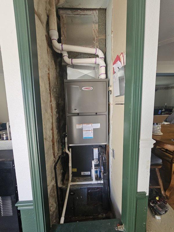 Completed installation of a Lennox Merit ML296V 96% AFUE 90,000 BTU two-stage gas furnace in residential utility closet. Installation included establishing new gas line connections with black iron pipe, running electrical service to unit, installing PVC venting system for intake and exhaust, and mounting programmable thermostat on interior wall for system control.