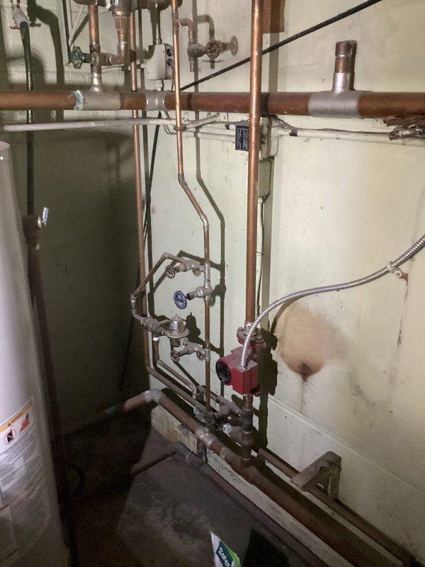 Conducted on-site assessment of existing residential boiler system in basement mechanical room to provide replacement estimate. The current unit is an older gray-green boiler with visible age-related wear, connected to copper piping distribution system and integrated with existing water heater. Evaluated the complete heating system infrastructure including supply and return piping, zone valves, circulation components, and venting requirements. Documented equipment specifications, spatial constraints, and existing plumbing configuration to determine appropriate replacement unit sizing and installation requirements. Photographed current installation to support equipment selection and project planning for the proposed boiler replacement.