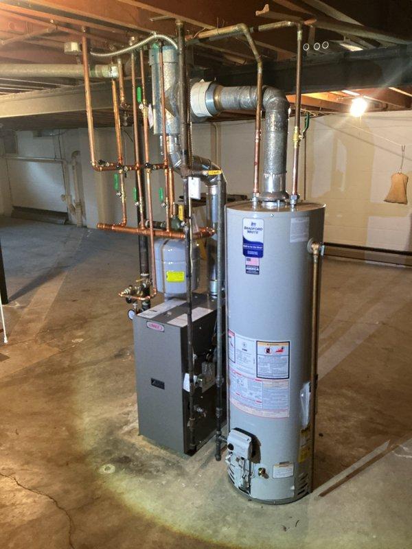 Completed installation of a 40-gallon slim Bradford White water heater in basement utility area. Connected all supply and discharge plumbing lines with copper piping, installed required shut-off valves, and integrated ventilation ductwork to existing HVAC system. Installation included proper venting configuration, safety valve installation, and verification of all connections for secure operation.
