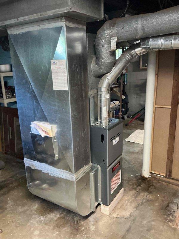 Performed a seasonal tune-up and inspection on a gas furnace, including a review of the flue venting connection, ductwork, and plenum seams, with foil-taped joints confirmed intact. Inspected surrounding equipment area and documented system condition; noted damp staining on the concrete floor near the furnace base and ductwork, and recommended monitoring for moisture or condensate sources.