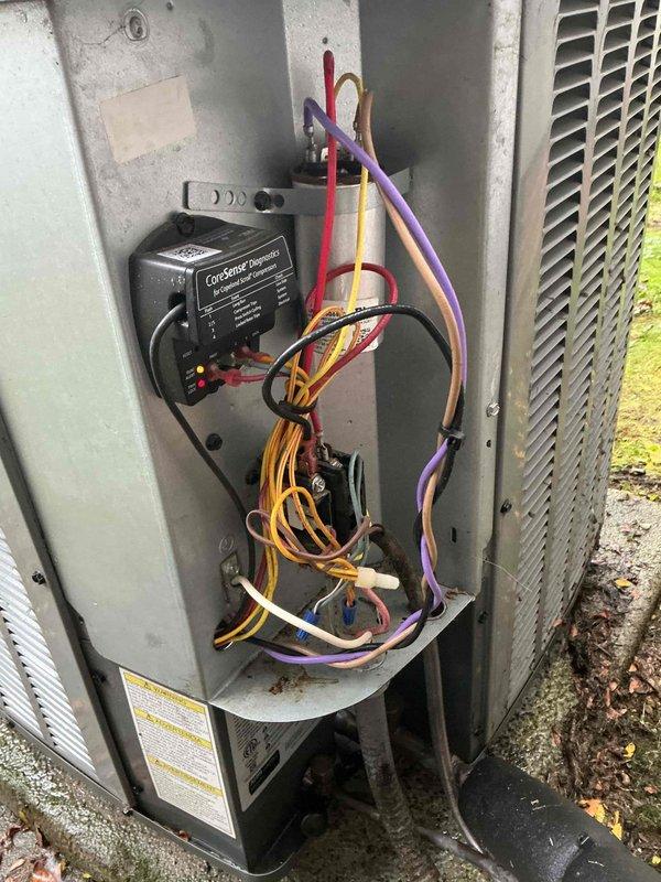 Performed seasonal cooling maintenance on an Amana split-system condenser, including inspection of the electrical compartment, contactor, run capacitor, and wiring connections, as well as the CoreSense compressor diagnostics module. Checked the unit's overall condition, noting moss and algae buildup on the concrete pad and minor corrosion on the base bracket, and confirmed the system is operating properly.