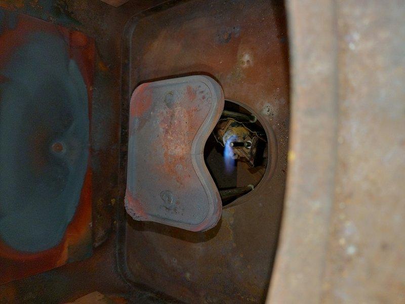 Performed a routine furnace tune-up and inspected the combustion chamber, pilot assembly, and burner compartment. Verified the pilot flame was lit and burning blue, and documented significant corrosion and heat-related discoloration on the interior combustion chamber surfaces and cover plate. System was operating properly at time of service; recommend monitoring the corrosion and evaluating the unit for potential replacement given its unknown age and condition.