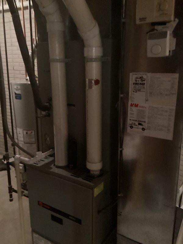 Performed an on-site evaluation for full replacement of two HVAC systems, inspecting the existing Trane gas furnace in the basement utility area, including its PVC venting, plenum and ductwork connections, and condensate drain, and documenting equipment condition and installation layout with photographs. Verified clearances and proximity to the adjacent water heater to determine system sizing and installation requirements for the replacement of both systems.