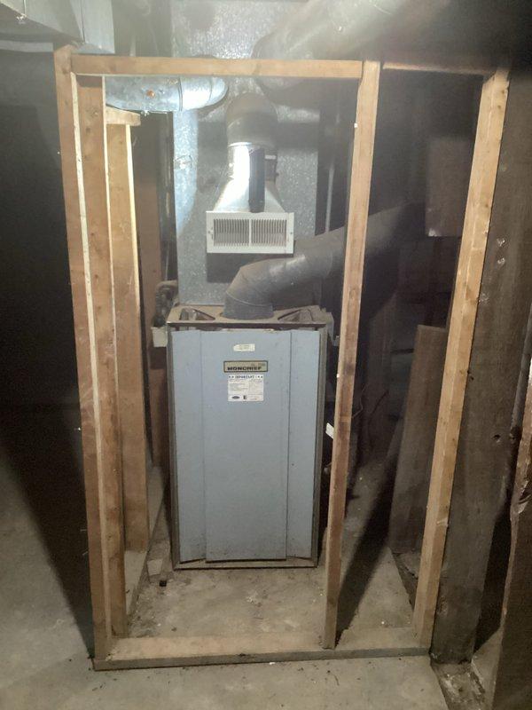 Performed an on-site evaluation for replacement of an existing Moncrief upright gas furnace located in an unfinished basement utility space. Inspected the furnace cabinet, supply plenum, galvanized ductwork, and flexible duct connections, documenting equipment condition and installation clearances with photographs. Existing unit shows age-related dust accumulation with no visible frost or major corrosion, and the documented findings were used to determine replacement scope and sizing.