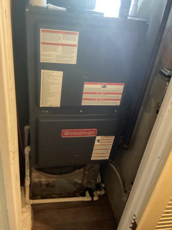 Performed an on-site replacement estimate for an existing downflow Goodman gas furnace installed in a closet, with a possible add-on or replacement of the air conditioning system. Inspected the cabinet, PVC condensate drain assembly with trap, flexible electrical conduit, and return-air filter section, noting debris in the condensate drain area and documenting existing conditions with photographs to determine equipment sizing and replacement scope.