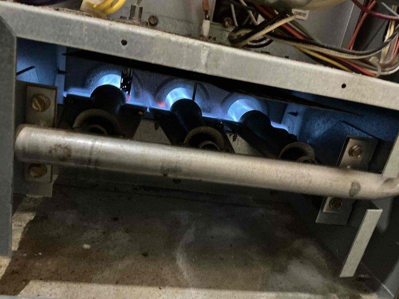Responded to complaint of furnace short cycling and reduced heating efficiency; inspected the Armstrong Air gas furnace and observed the burner assembly firing with a stable blue flame across all burners. Evaluated the venting and combustion components, including the galvanized flue connection to the water heater vent, as part of the short-cycling diagnosis, and noted dirty burner compartment with debris and residue. Furnace was left operating and cycling through the heat call.