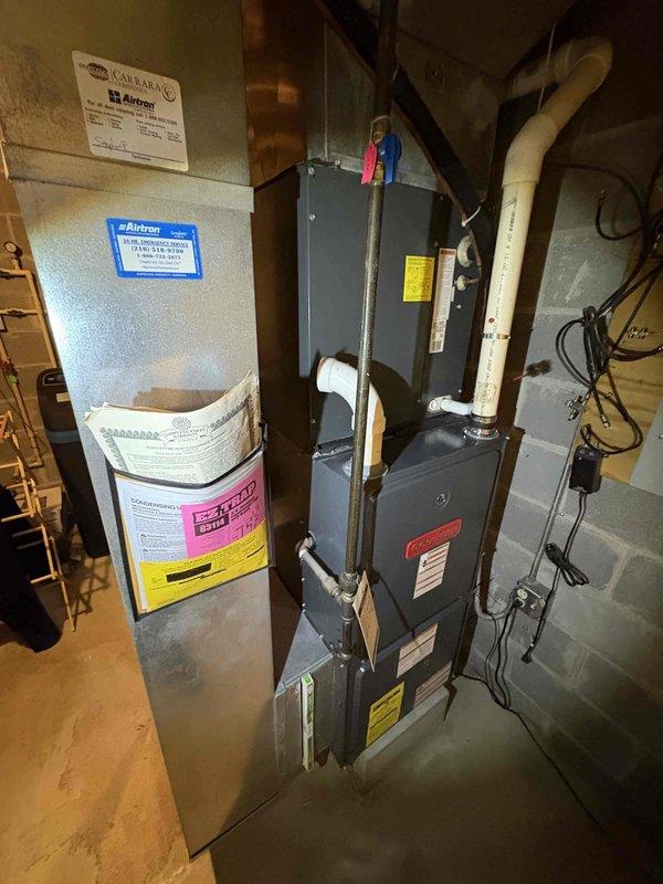 Completed furnace replacement estimate, documenting existing installation in basement utility area consisting of furnace unit with connected air handler/heat pump system. System features standard PVC drainage pipes, metal ductwork, and proper electrical connections mounted against concrete wall. Exterior inspection revealed snow-covered condenser unit positioned on concrete pad adjacent to vinyl-sided exterior wall.