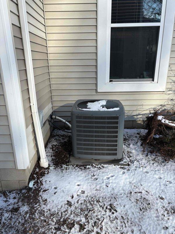 Completed furnace replacement estimate, documenting existing installation in basement utility area consisting of furnace unit with connected air handler/heat pump system. System features standard PVC drainage pipes, metal ductwork, and proper electrical connections mounted against concrete wall. Exterior inspection revealed snow-covered condenser unit positioned on concrete pad adjacent to vinyl-sided exterior wall.