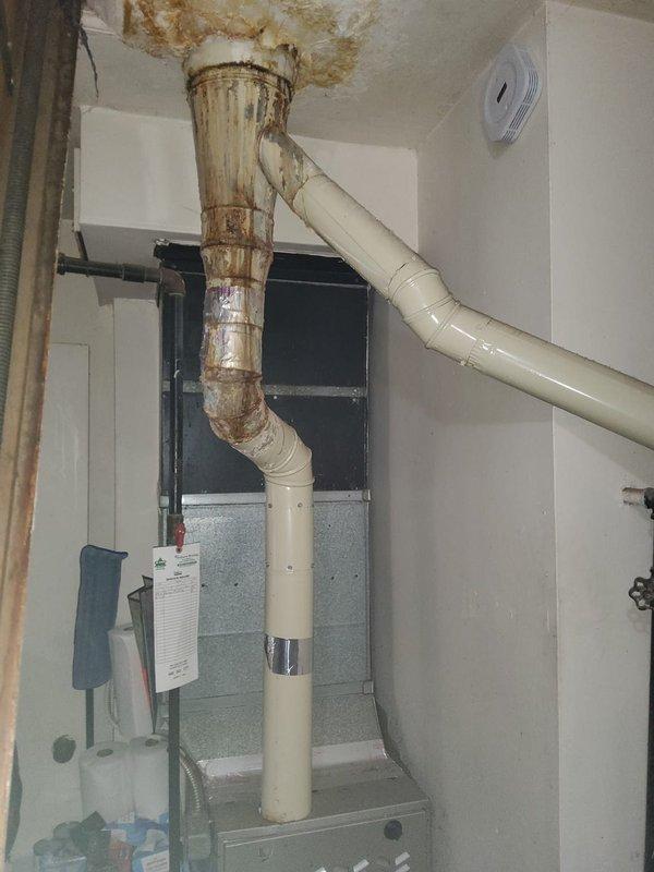 Responded to service call for furnace condensation leak. Inspection revealed significant corrosion and water damage at the metal-to-PVC transition in the exhaust flue system. Observed rust deterioration at the ceiling connection point with evidence of ongoing moisture issues. Structural inspection of surrounding support elements showed some water staining on wooden components, indicating prolonged exposure to condensation.