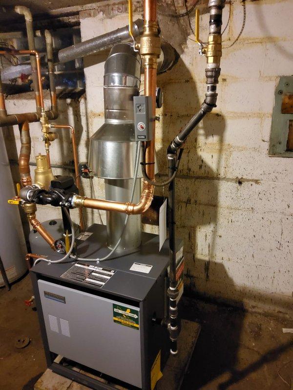Completed installation of new hot water boiler system including expansion tank, backflow/PRV combo, pump, vertical air eliminator, and 2" inline air separator with thermostat. Removed old ceiling-mounted expansion tank and connected to existing 2" copper piping. System properly vented with metal flue and all components securely mounted with appropriate valves and pressure gauges.