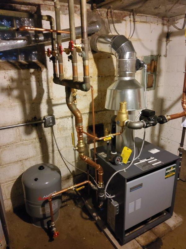 Completed installation of new hot water boiler system including expansion tank, backflow/PRV combo, pump, vertical air eliminator, and 2" inline air separator with thermostat. Removed old ceiling-mounted expansion tank and connected to existing 2" copper piping. System properly vented with metal flue and all components securely mounted with appropriate valves and pressure gauges.