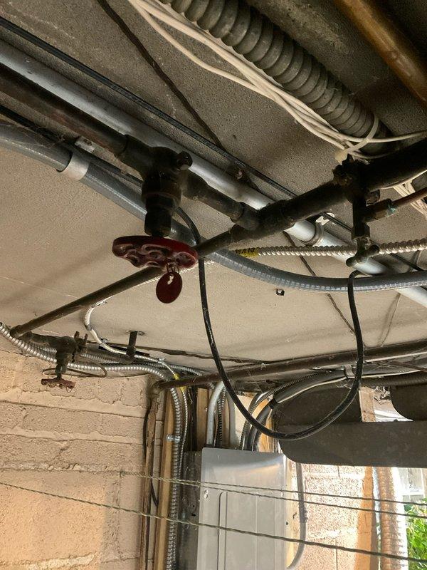 Conducted plumbing assessment of basement utility area, documenting exposed plumbing infrastructure including main shut-off valve and associated piping. Identified significant structural deterioration around insulated pipe, with evidence of moisture damage, torn insulation, and possible corrosion at wall junction near glass block window. Photos taken to document current condition for further evaluation.