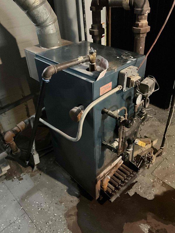 Inspected aging boiler system that was previously serviced in November and reported as non-functional again. Visual examination revealed an older blue-green heating unit with signs of wear and connected galvanized exhaust ducting. Evaluated control components, burner assembly, valves, and various copper/metal pipe connections for proper operation prior to anticipated storm conditions.