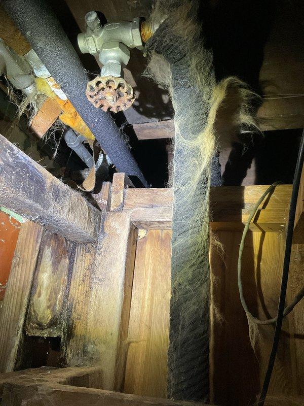 Responded to emergency call for burst pipe in basement causing water backup issues. Inspection of the crawlspace revealed significant corrosion on water supply lines and valve assembly with extensive cobweb accumulation indicating long-term moisture exposure. Replaced damaged pipe section and restored proper water flow while ensuring no additional leakage into hot water heater.
