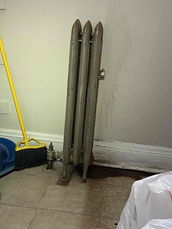 Inspected 15-20 year old boiler system with multiple radiators showing leakage issues. Observed water level in sight glass indicating system is full. Documented cast iron radiators with visible corrosion and potential water damage at mounting points, particularly noting deterioration around valve connections and floor staining beneath units.