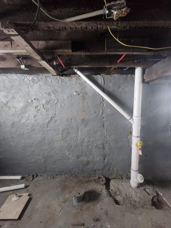 Conducted inspection of property's plumbing system to prepare quote for waterline and drain replacement. Examined exposed PVC drainage system in basement/crawl space area with dirt floor and concrete walls. Also assessed ceiling-mounted PVC plumbing infrastructure with multiple connection points and joints that showed evidence of purple primer application. Photos documented current installation to support detailed replacement quote.