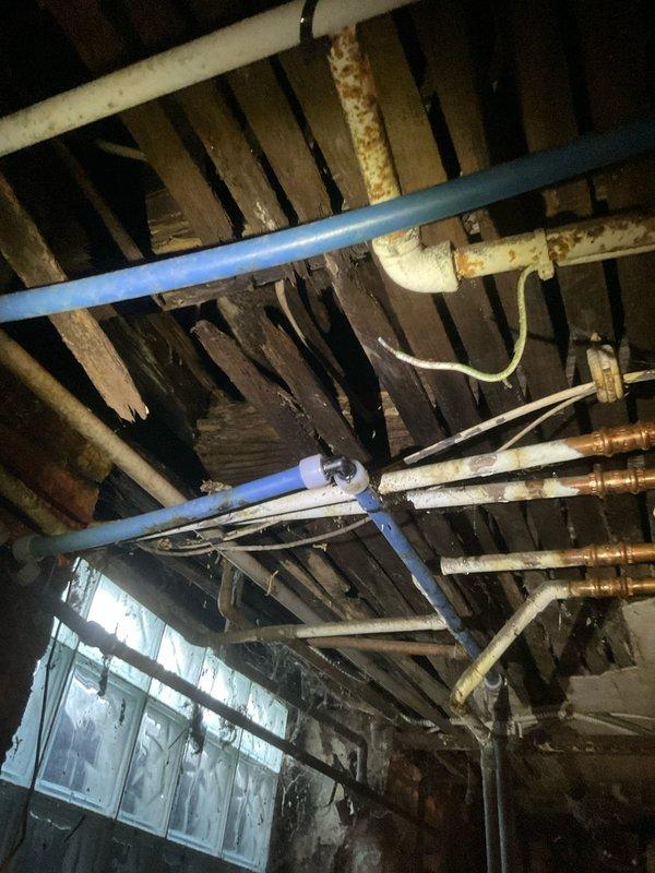 Performed inspection of aging plumbing system in crawl space/basement area. Observed multiple copper pipes showing significant corrosion and deterioration alongside PVC piping. Identified potential water damage to wooden joists in ceiling structure. Visual assessment completed to determine necessary repairs for future service.