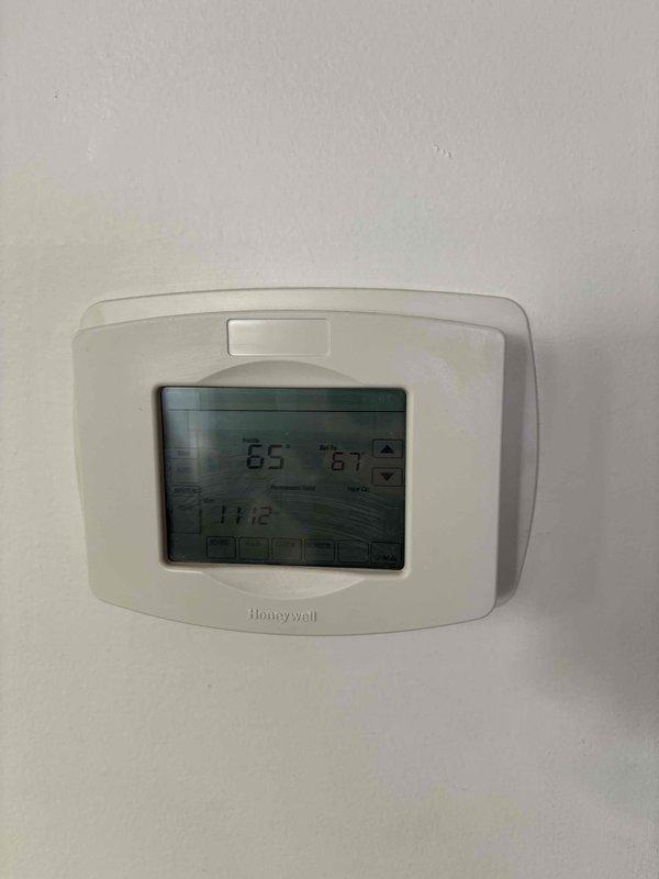 Responded to heating issue service call. Inspected Honeywell digital thermostat system showing 65°F current temperature with 67°F target setting. Examined basement ductwork system, noting metal panels with proper insulation and connection points. Recommended replacement of aging furnace unit to resolve ongoing heating performance concerns.