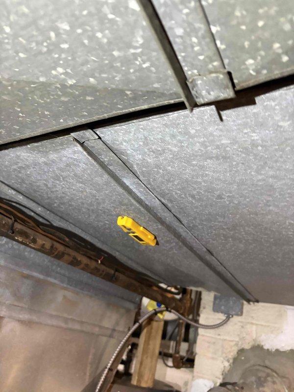 Responded to heating issue service call. Inspected Honeywell digital thermostat system showing 65°F current temperature with 67°F target setting. Examined basement ductwork system, noting metal panels with proper insulation and connection points. Recommended replacement of aging furnace unit to resolve ongoing heating performance concerns.