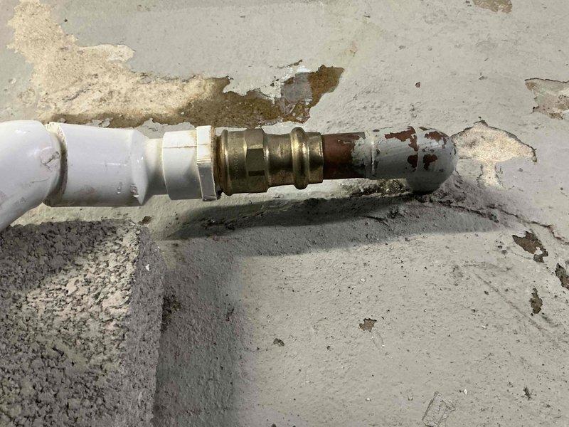 Responded to water leak service call for 7-year-old furnace. Discovered broken humidifier discharge pipe with significant deterioration at connection point between PVC and brass fitting. Replaced damaged section and secured proper drainage to prevent further moisture damage to concrete floor, which showed signs of previous water exposure and mineral deposits.