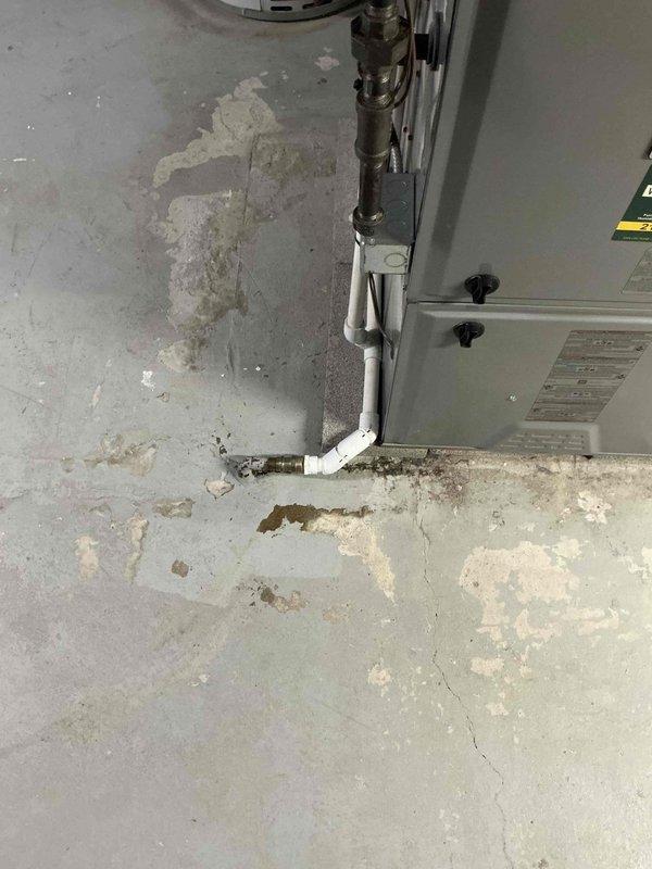 Responded to water leak service call for 7-year-old furnace. Discovered broken humidifier discharge pipe with significant deterioration at connection point between PVC and brass fitting. Replaced damaged section and secured proper drainage to prevent further moisture damage to concrete floor, which showed signs of previous water exposure and mineral deposits.