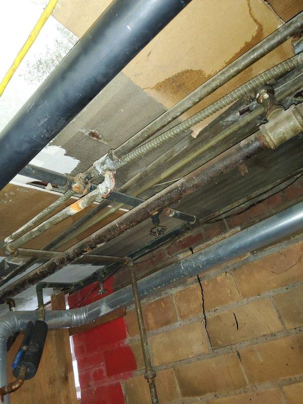 Inspected leaking stack behind recently installed boiler. Observed significant corrosion and water damage at connection points of cast iron waste pipe and copper supply lines. Documented evidence of ceiling water staining and pipe deterioration, recommending complete replacement of affected section to prevent further leakage and structural damage.