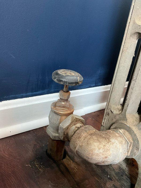 Responded to service call for 1938 steam radiator system requiring repair. Inspected aged plumbing components including main water valve and connecting pipes showing significant wear. Serviced door-adjacent radiator assembly and restored proper functionality to the vintage heating system.