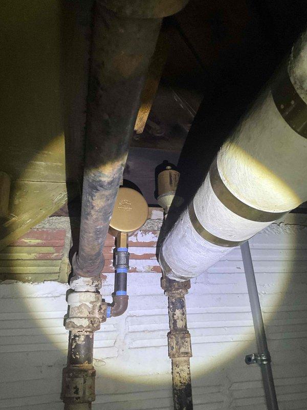 Conducted comprehensive evaluation of steam boiler system with severely compromised heat exchanger, exhibiting significant damage on both sides. Documentation of basement utility room revealed exposed ductwork, control systems, and plumbing infrastructure with visible corrosion at connection points, particularly in the brass valve assembly.