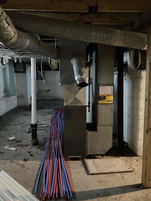 Conducted assessment for HVAC system replacement in three-story home currently using dual furnace setup. Client prefers consolidation to single furnace if feasible. Inspection of basement revealed existing furnace with deteriorating ductwork and inadequate insulation. Third floor will require new ductwork installation. Photos documented current system configuration including metal ductwork, PEX plumbing proximity, and overall mechanical space conditions.